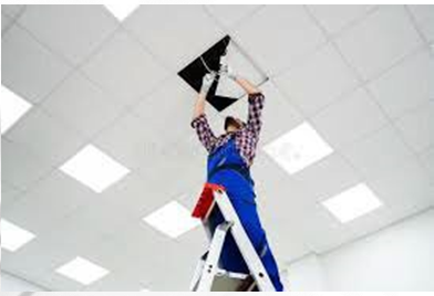 Das Bild zeigt einen Handwerker auf einer Stehleiter, der eine Elektroleitung an einer Kassettendecke installiert.