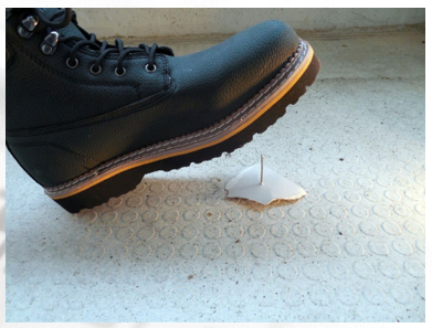 Das Bild zeigt einen Schuh der auf einen Nagel am Boden tritt.